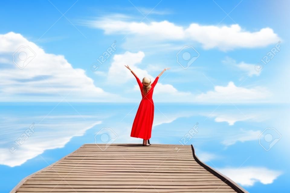 Летний день. Улыбающиеся женщины расслабляются и носят красную одежду моды, стоя на деревянном мосту над морем, фоне голубого неба. Путешествия и отдых. Концепция свободы