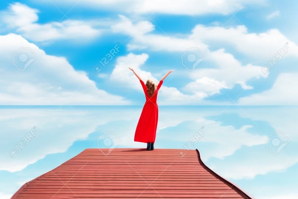 Летний день. Улыбающиеся женщины расслабляются и носят красную одежду моды, стоя на деревянном мосту над морем, фоне голубого неба. Путешествия и отдых. Концепция свободы