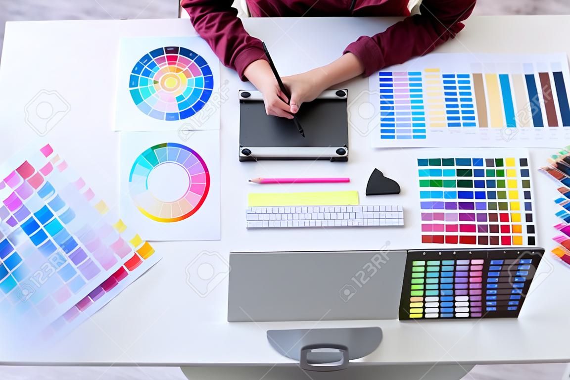 Bild einer kreativen Grafikdesignerin, die an der Farbauswahl arbeitet und am Arbeitsplatz auf einem Grafiktablett zeichnet, Arbeitsbereich von oben.