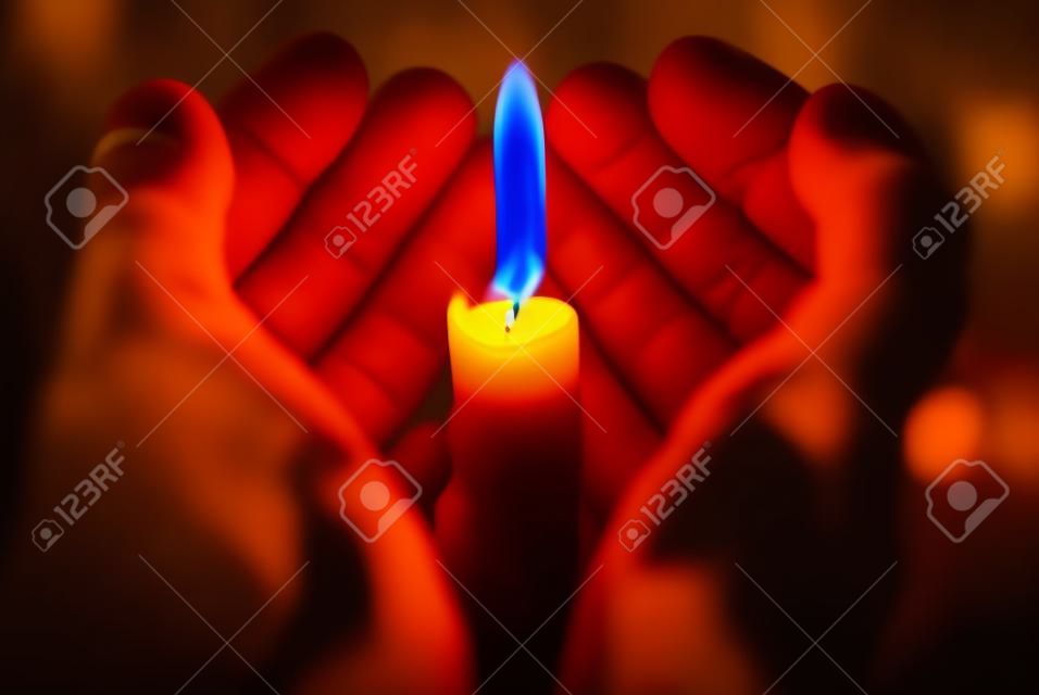 hands holding a burning candle in dark
