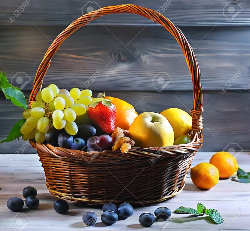 Panier en paille en osier avec un assortiment de fruits et de citron, orange, raisin, fraise, baies Physalis, mandarine sur une table en bois dans un style rustique