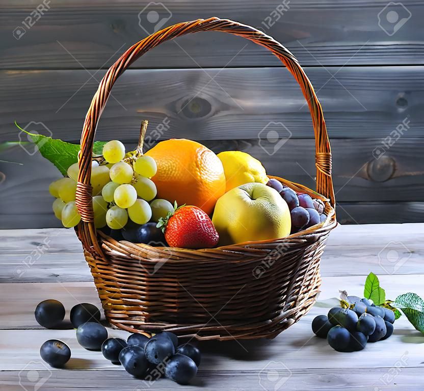 Panier en paille en osier avec un assortiment de fruits et de citron, orange, raisin, fraise, baies Physalis, mandarine sur une table en bois dans un style rustique