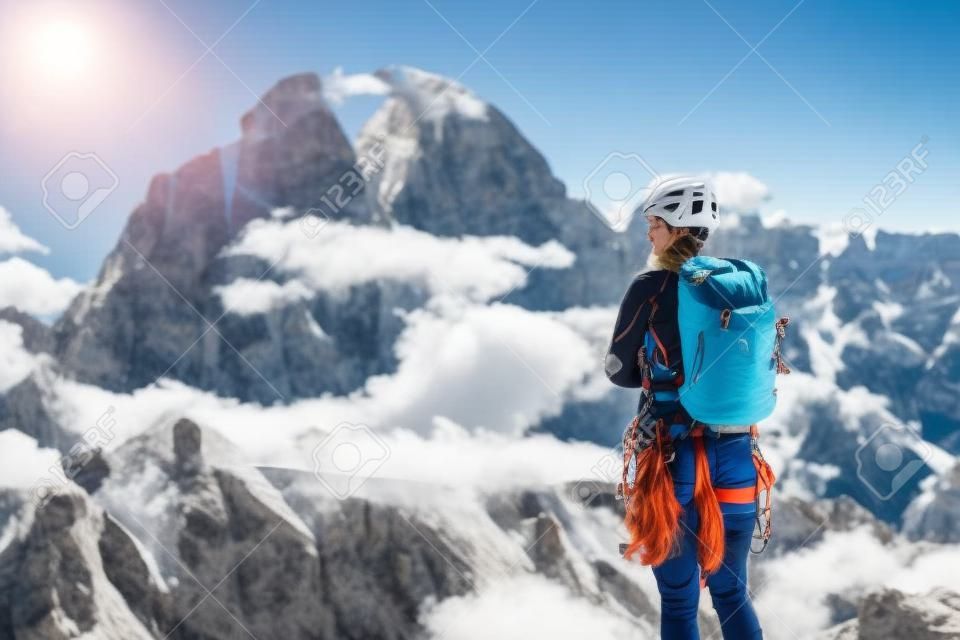 Female mountaineer with backpack, helmet and harness with climbing gear enjoying stunning view to mount Tofana di Rozes before ascent during summer day in Dolomite Alps - adventure concept