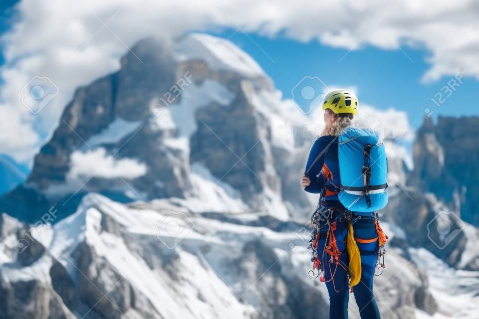 Female mountaineer with backpack, helmet and harness with climbing gear enjoying stunning view to mount Tofana di Rozes before ascent during summer day in Dolomite Alps - adventure concept