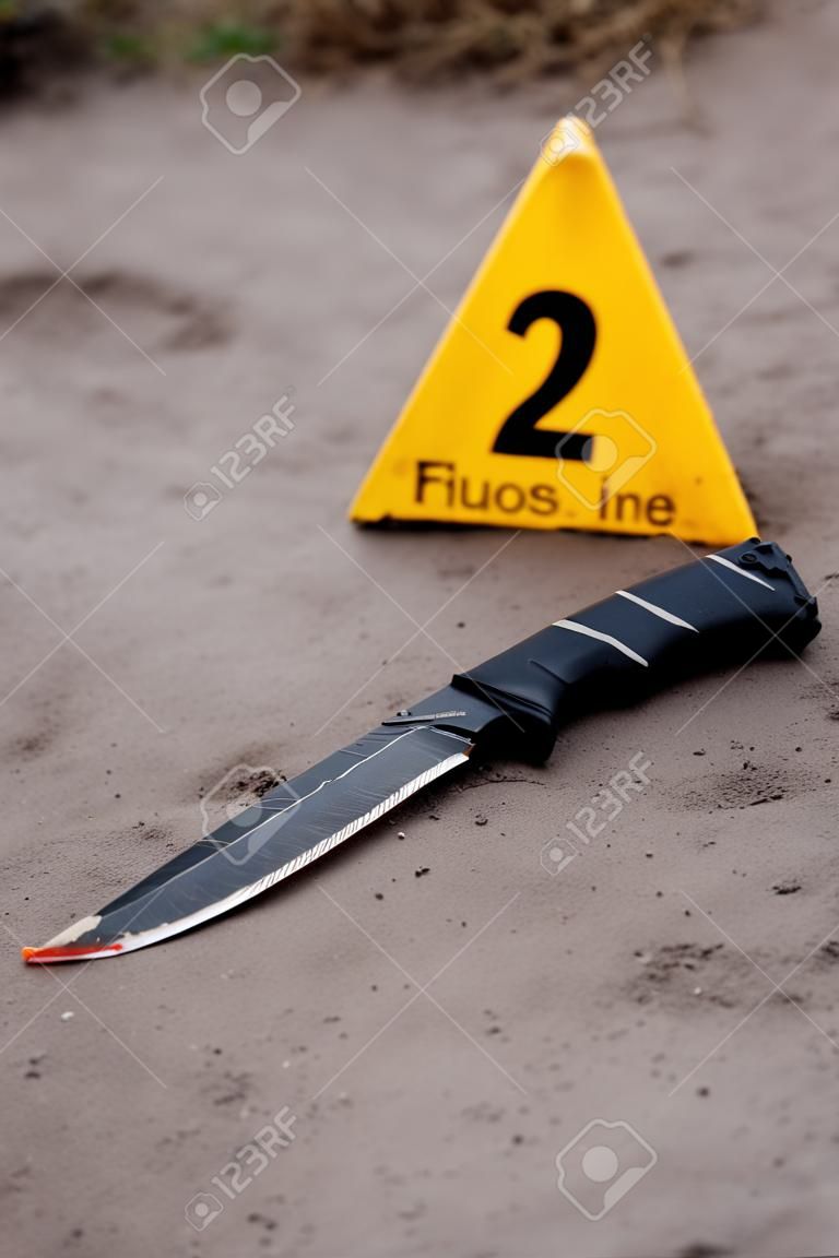Investigação da cena do crime, faca sangrenta com marcadores de crime no chão, provas de homicídio.