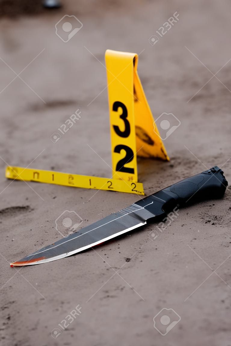 Investigação da cena do crime, faca sangrenta com marcadores de crime no chão, provas de homicídio.