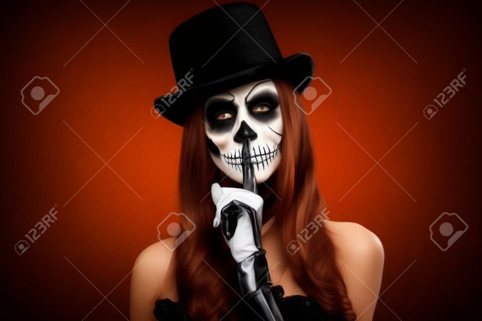 Mulher em silêncio de Halloween. Uma mulher em chapéu de topo e crânio compõem.