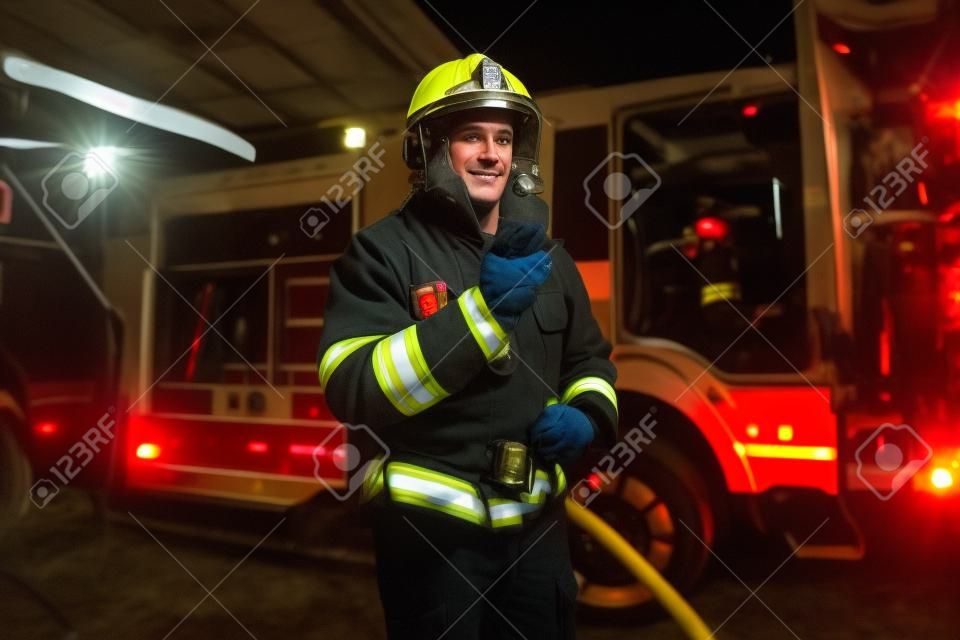 De brandweer arriveerde's nachts. Brandweerman in een beschermend uniform naast een brandweerwagen en praat op de radio.