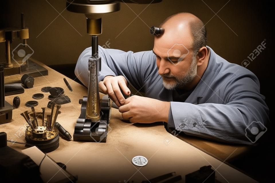 Reifer Uhrmacher graviert für Kundenuhren in seiner Werkstatt.