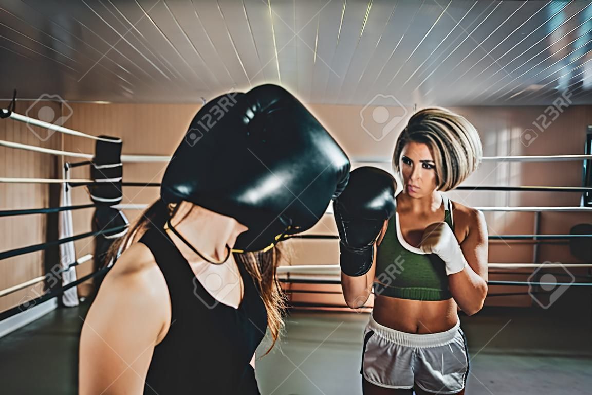 Boxing coach and her trainee have a sparring on the ring at special gym.
