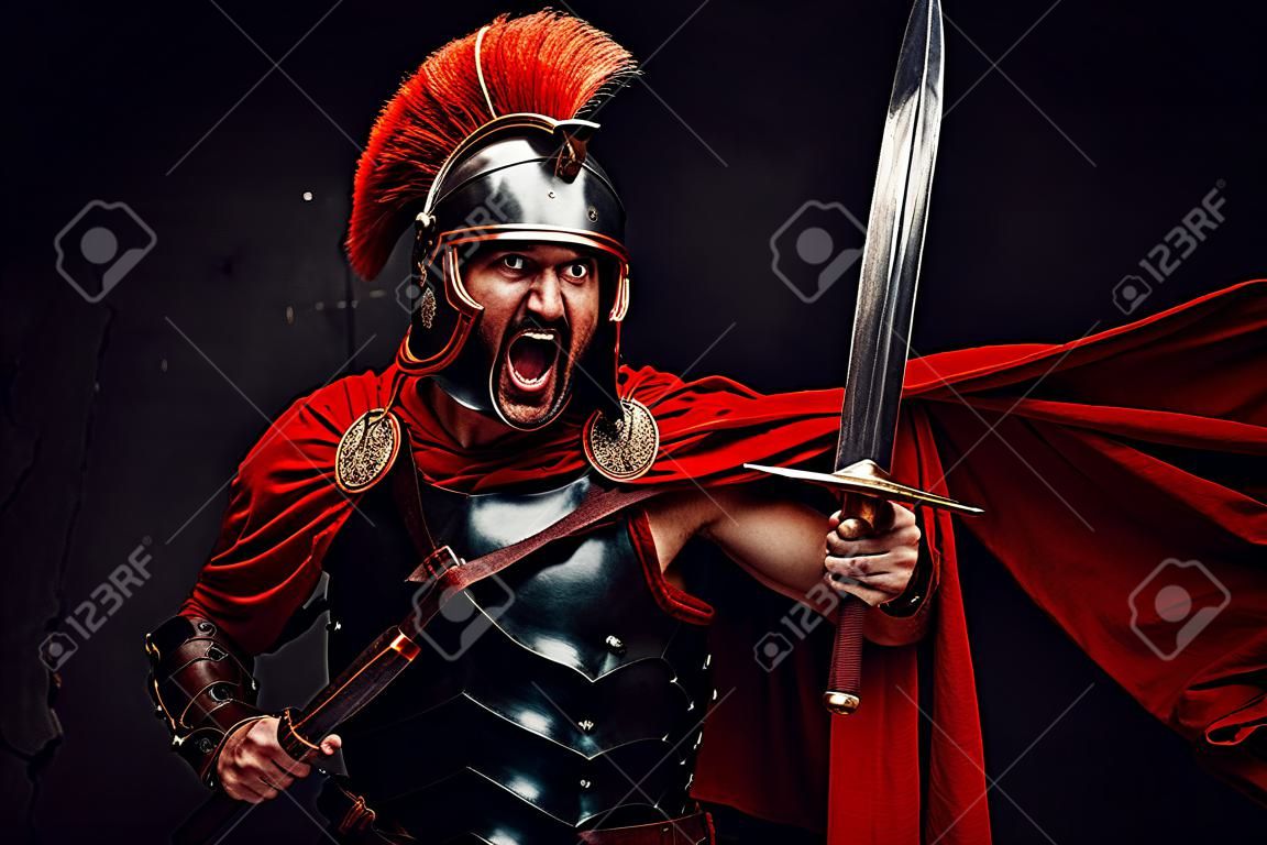 Atacando a un salvaje y brutal soldado imperial de Roma con armadura de acero y capa roja sosteniendo espada y escudo en un fondo oscuro.