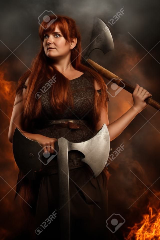 Armoured scandinavian lady with long brown hairs holding two huge axes in atmospheric smokey background.