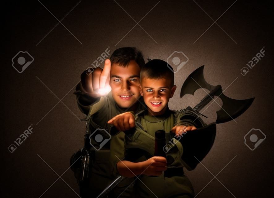 Military boy and his father warrior behind him pointning a finger at camera in dark background.