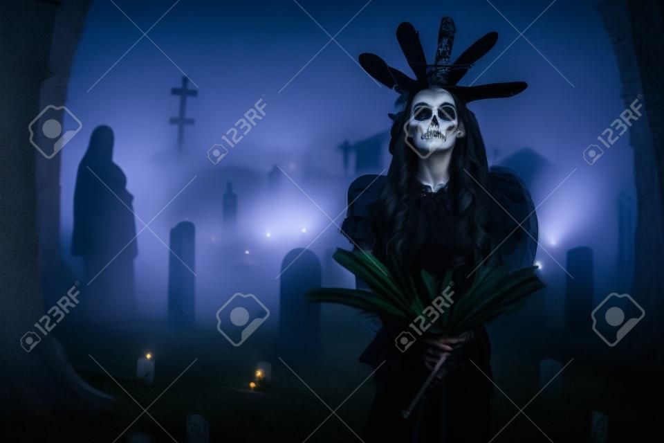 Spooky witch with staff in cemetery with fog at night