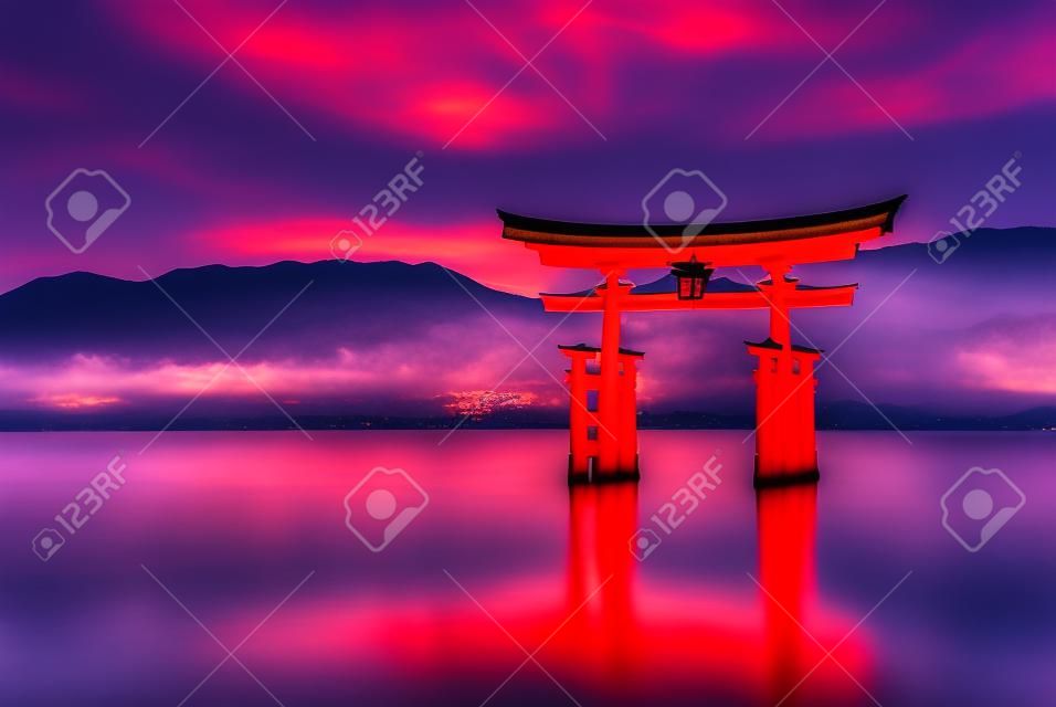 Wielka pływająca brama (o-torii) odbijająca się w wodzie na wyspie miyajima w pobliżu świątyni shinto okushima w japonii wkrótce po zachodzie słońca z dramatycznym żywym niebem