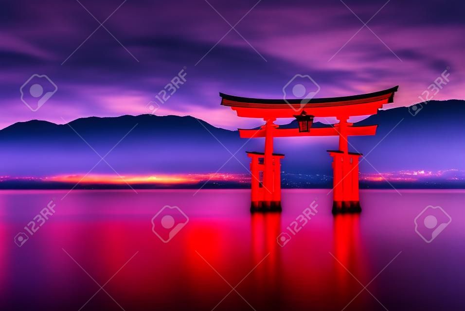 Wielka pływająca brama (o-torii) odbijająca się w wodzie na wyspie miyajima w pobliżu świątyni shinto okushima w japonii wkrótce po zachodzie słońca z dramatycznym żywym niebem