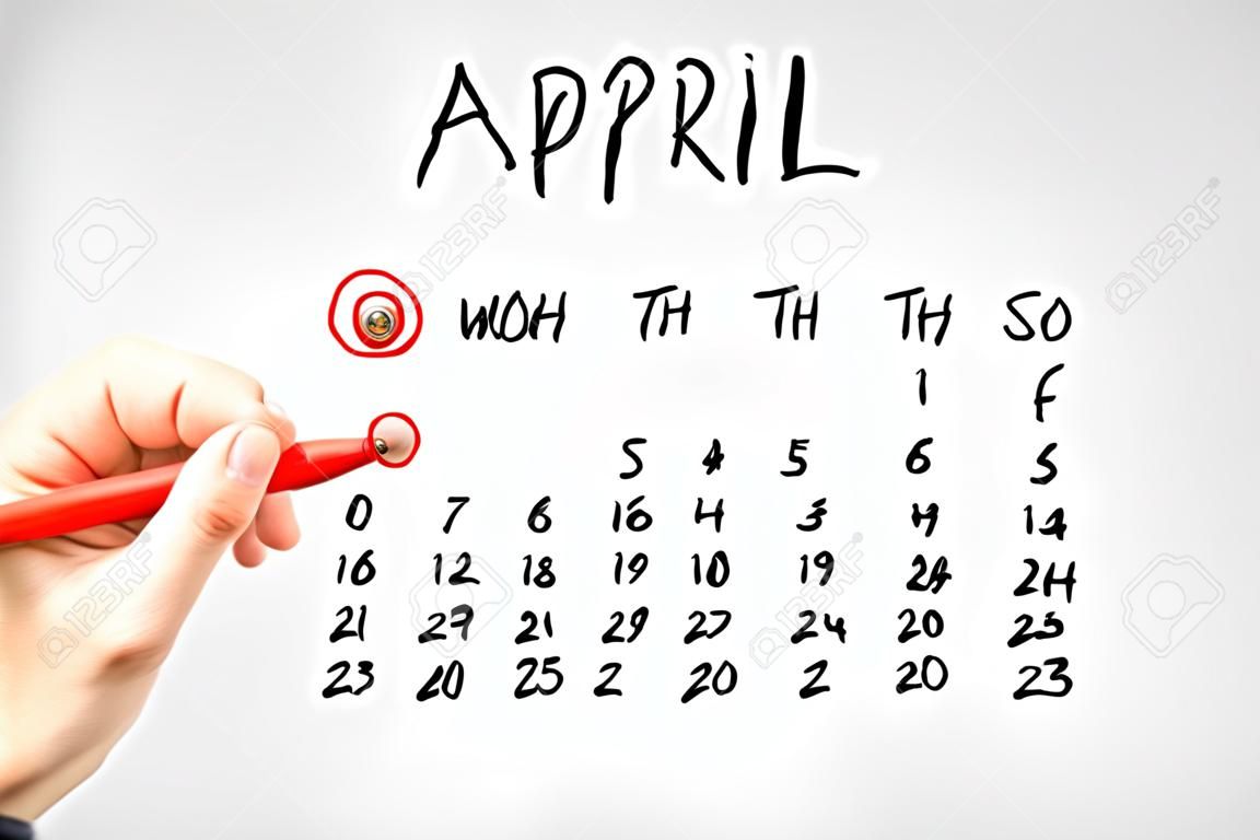 Hand drawn calendar for April on a virtual interface or screen with the First ringed in red by a man holding a marker pen, closeup of his hand. Fools day concept.