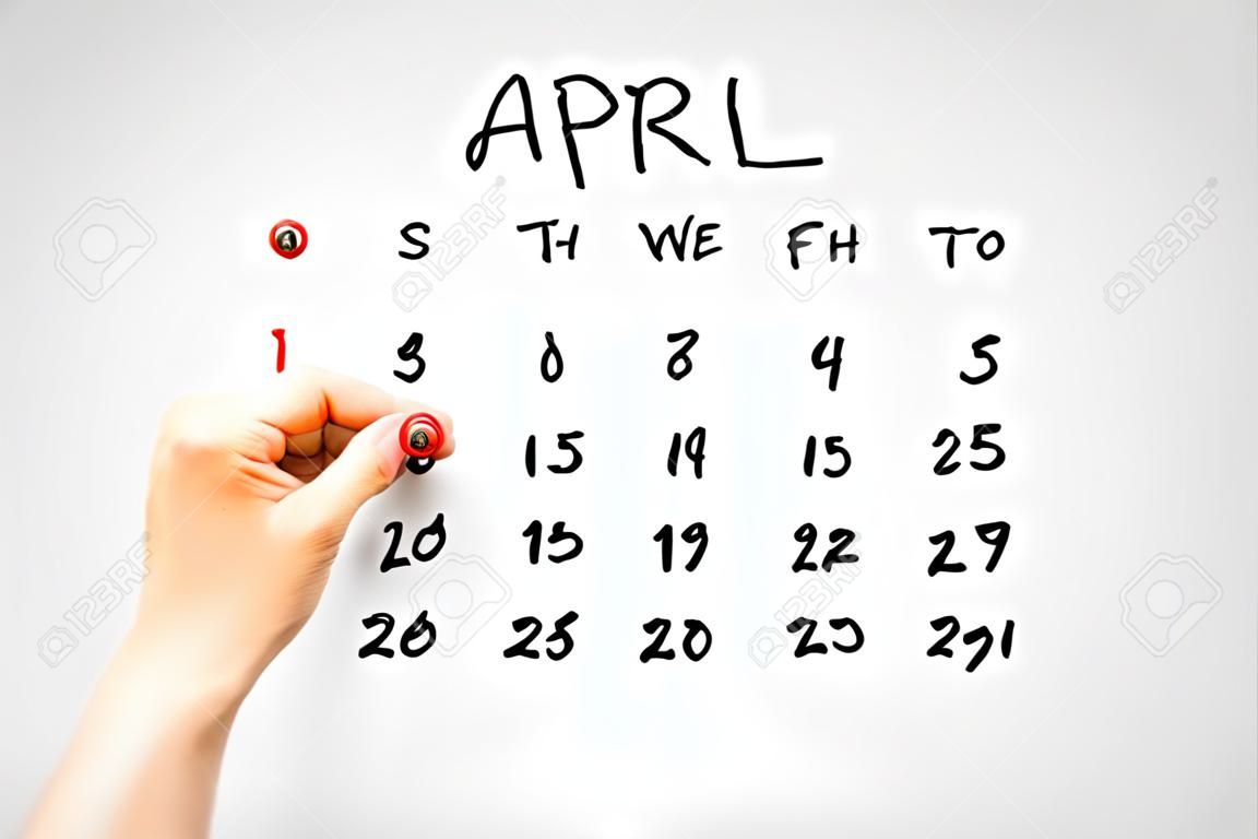 Hand getekende kalender voor april op een virtuele interface of scherm met de Eerste ringed in rood door een man met een marker pen, close-up van zijn hand. Dwazen dag concept.