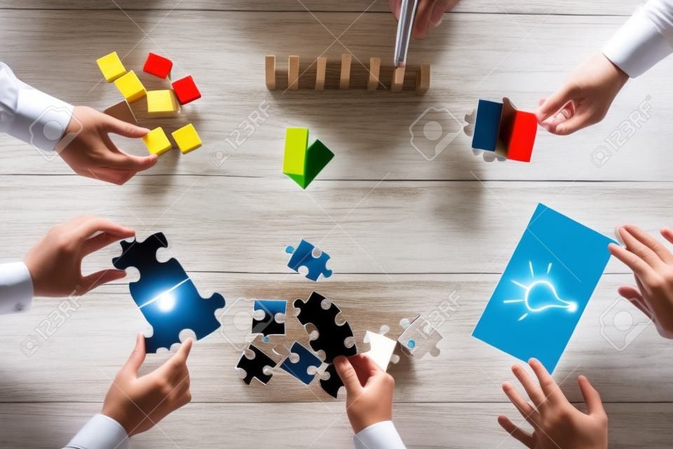 Geschäftsleute der Planung der Geschäftsstrategie und halten Puzzleteile, die Schaffung Ideen mit Glühbirne auf dem Papier und Neuordnung Holzblöcke erstellt. Konzeptionelle für Teamarbeit, Strategie, Vision oder Bildung.