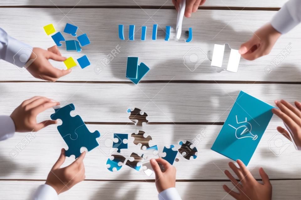 Üzletemberek tervezés üzleti stratégia, miközben a puzzle darabkái, ami a gondolatokat izzó rajzolt papírra és átrendezése fadarabot. Fogalmi csapatmunka, stratégia, jövőkép és az oktatás.