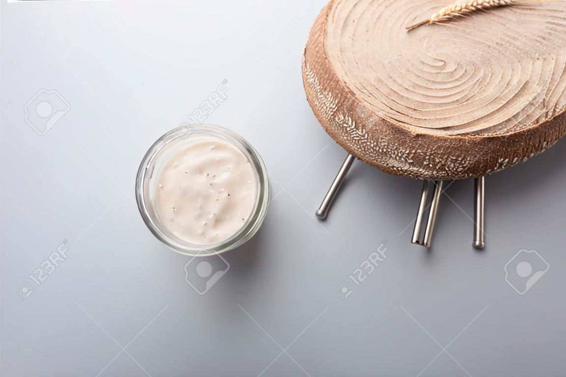 유리병에 있는 사워도우 스타터 효모와 회색 배경 위에 갓 구운 통밀 빵의 최고 전망.