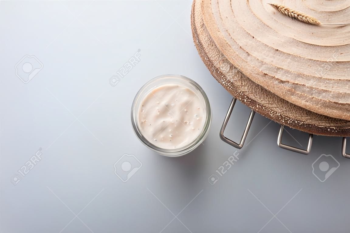 Top view of sourdough starter yeast in a glass jar and freshly baked wholewheat bread over grey background.