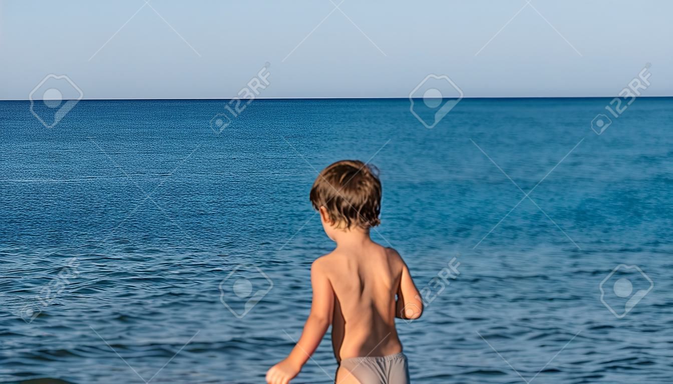 Toddler boy by a beautiful blue sea on a hot summer day.