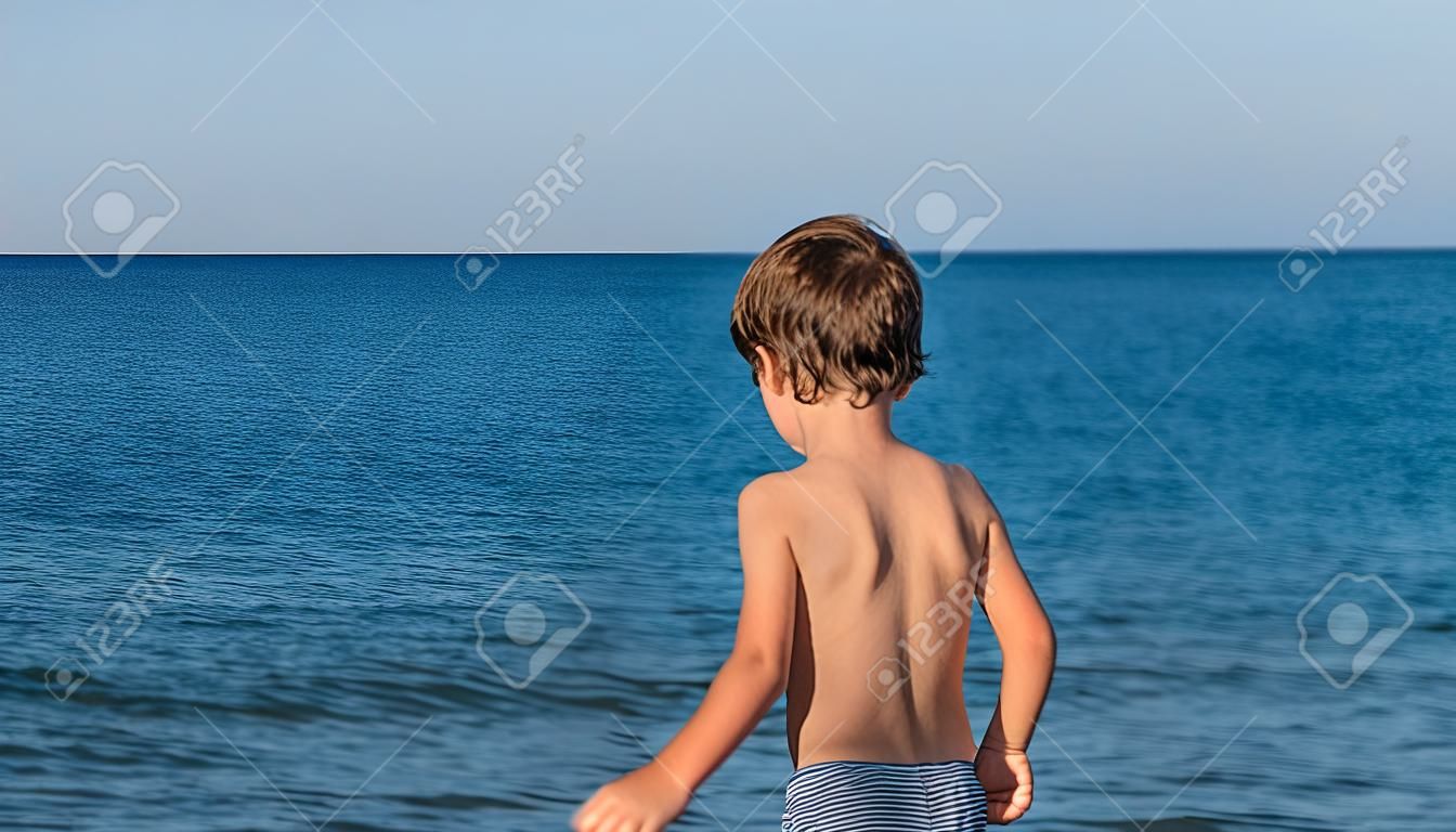 Toddler boy by a beautiful blue sea on a hot summer day.