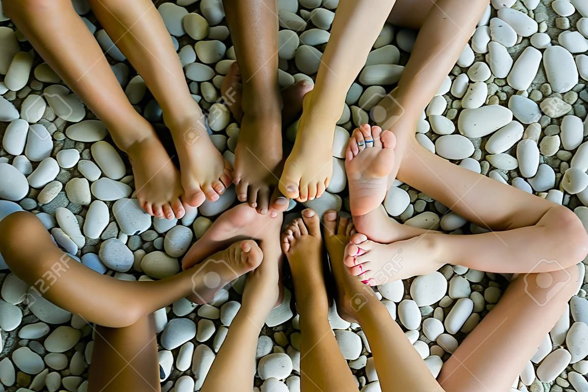 Top view of feet of five kids in a star shape on pebble beach.