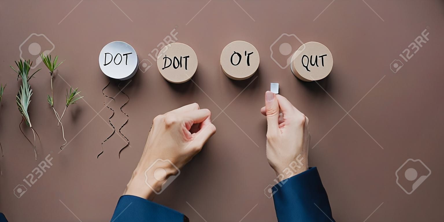 Top view of male and female hands assembling a Do it or Dont quit sign on wooden cut circles  in a conceptual image of business ambition and success. Over brown background.