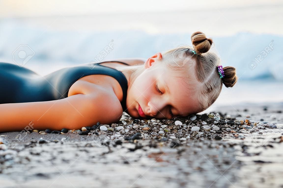 Una ragazza adolescente è seduta sulla spiaggia in costume da bagno nero.
