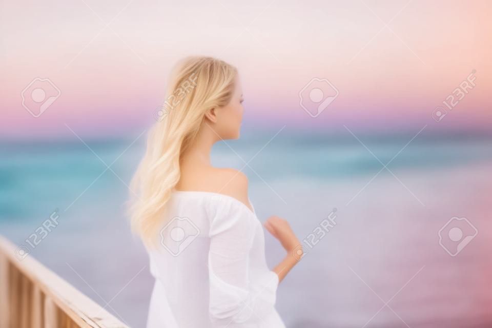 Hermosa joven rubia con camisa blanca en el muelle al atardecer. foto borrosa, fondo