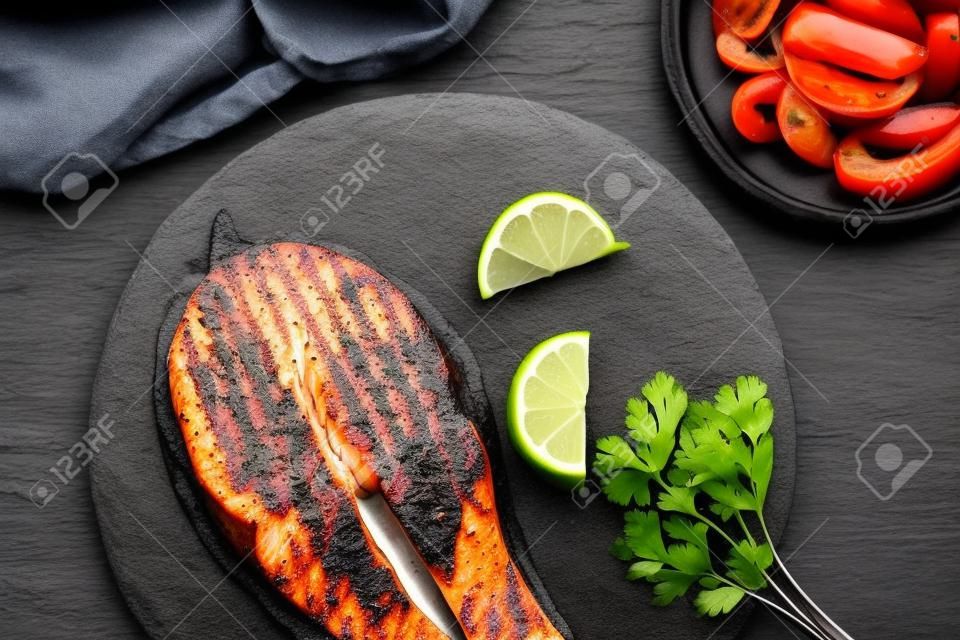 Trancio di salmone alla griglia su un piatto di ardesia nera con prezzemolo e lime