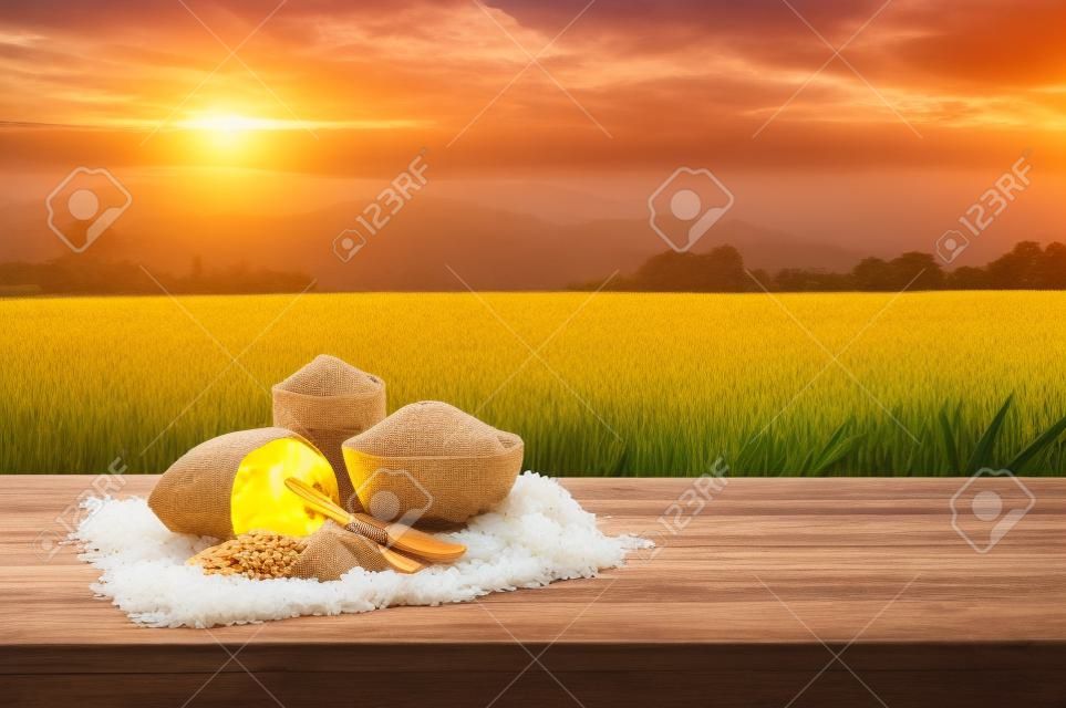 Asian uncooked white rice with the sunset rice field background and burlap sack on wooden table. rice grains healthy food