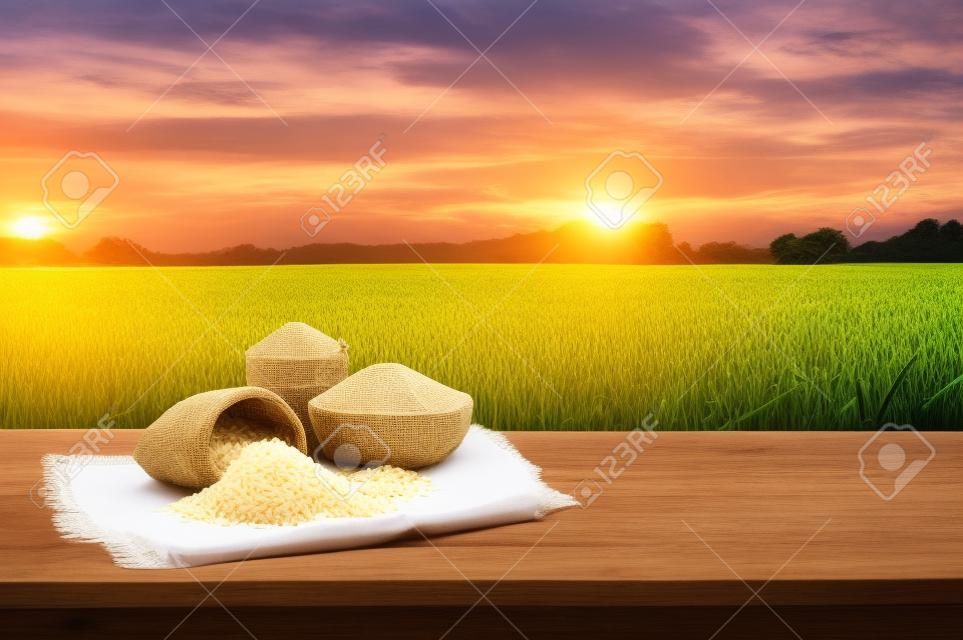 Asian uncooked white rice with the sunset rice field background and burlap sack on wooden table. rice grains healthy food
