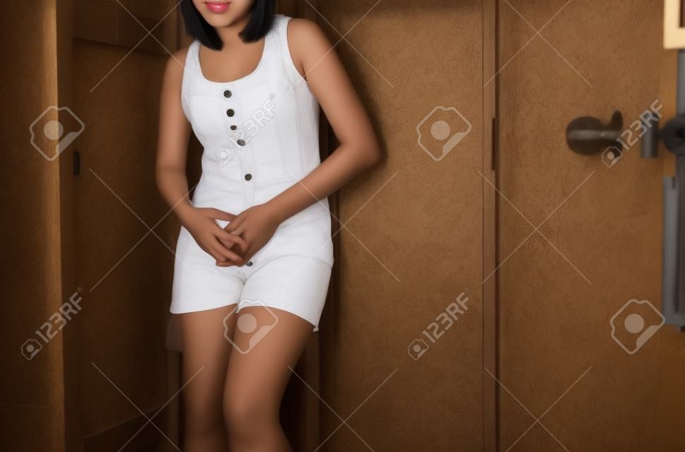 Mano mujer asiática sosteniendo su entrepierna, necesidad femenina de orinar en un inodoro