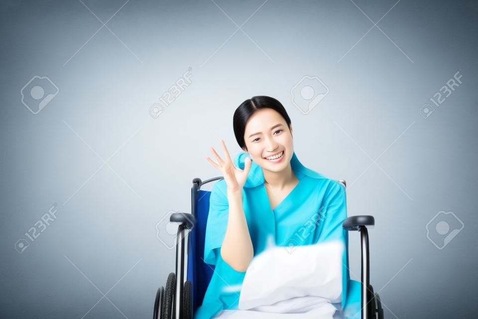 Aziatische mooie vrouw patiënten omhoog uw hand OK teken symbool en zitten op rolstoel in het ziekenhuis, gelukkig en glimlachen