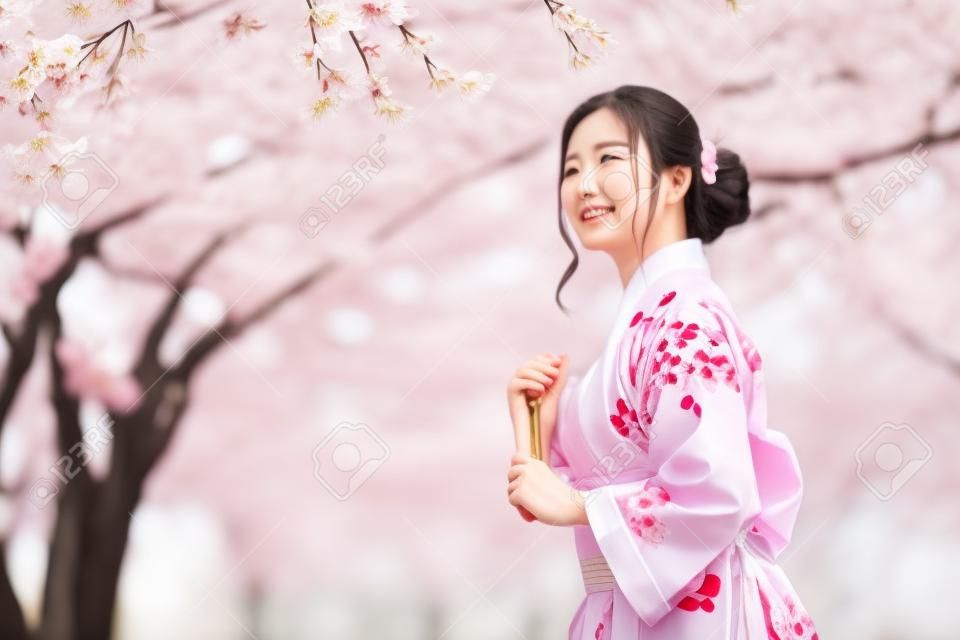 donna in yukata (abito kimono) con in mano un ventaglio pieghevole e guardando il fiore di sakura o il fiore di ciliegio che fiorisce nel giardino
