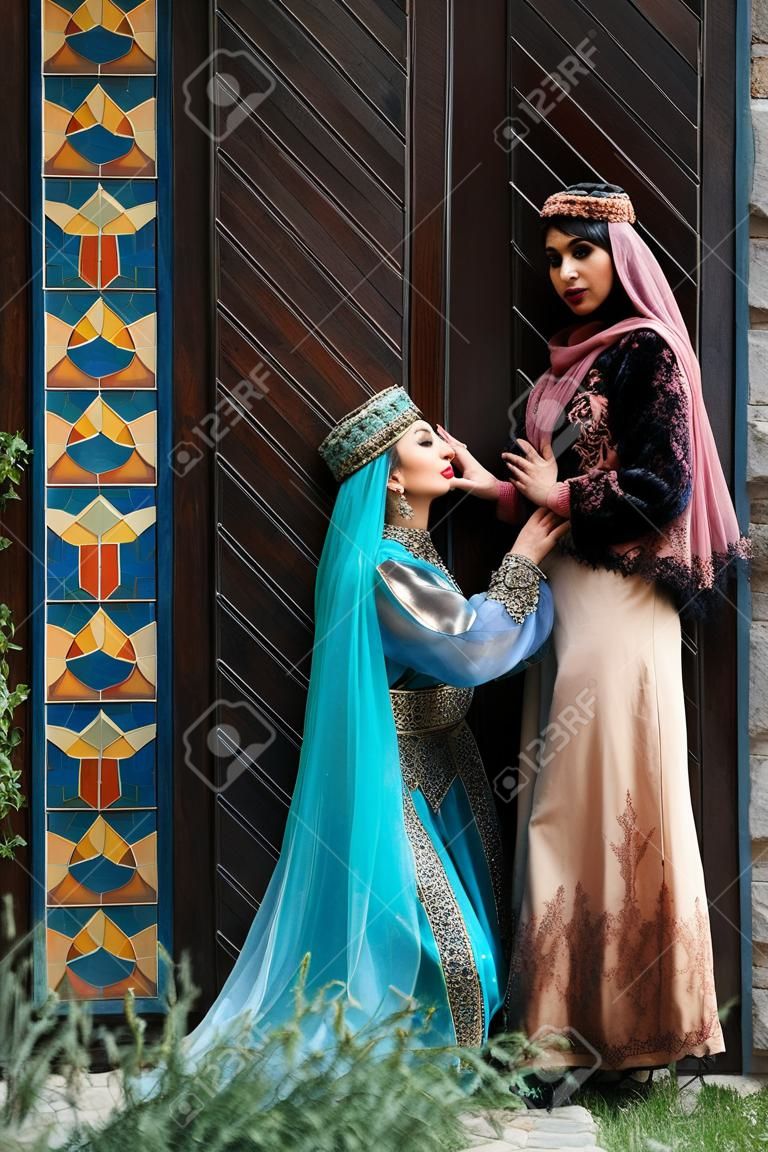 Belles femmes azéries en robe traditionnelle azerbaïdjanaise frappant la porte en bois d'une vieille maison. Printemps, concept de célébration des vacances de Novruz
