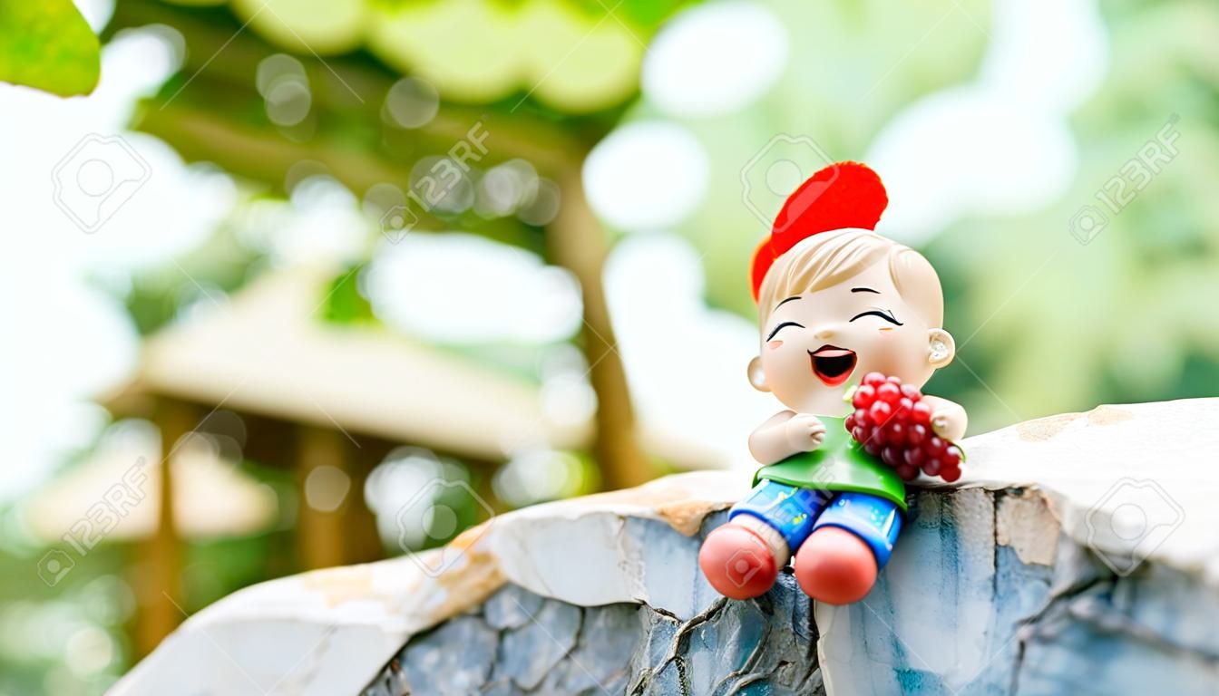 Plaster doll chinese girls smile with grape fruit that can be purchased in the market sitting on the rock with bokeh background.