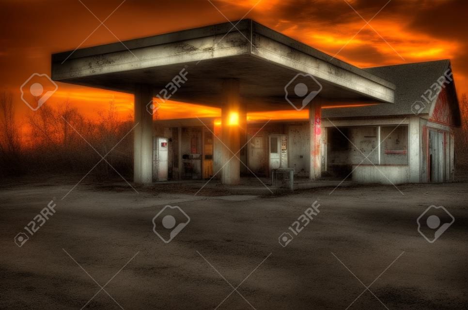 放棄されたフリーク古いガソリンスタンド、背景に日没。