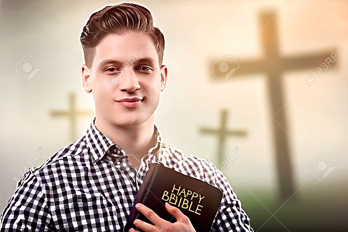 年輕英俊的快樂的人拿著一本聖經與樹十字架的背景（復活節概念）