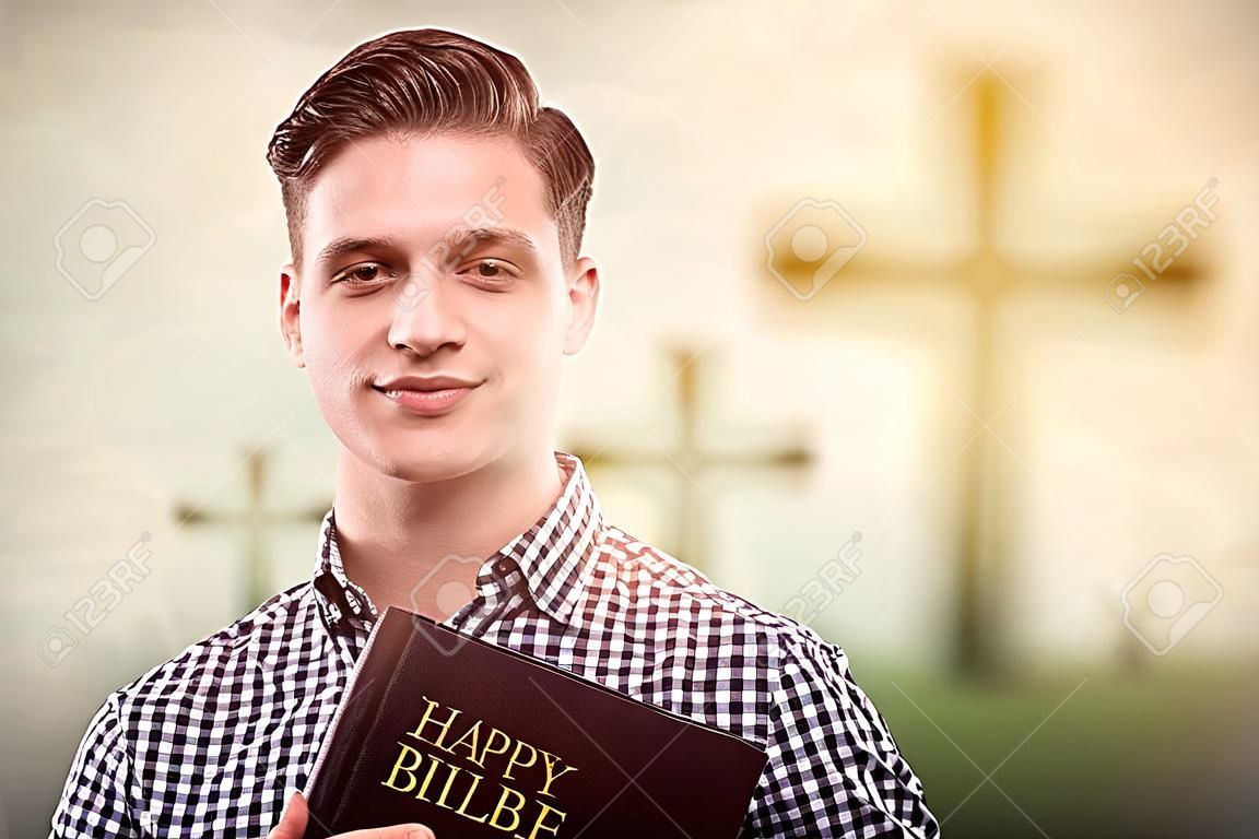 年輕英俊的快樂的人拿著一本聖經與樹十字架的背景（復活節概念）
