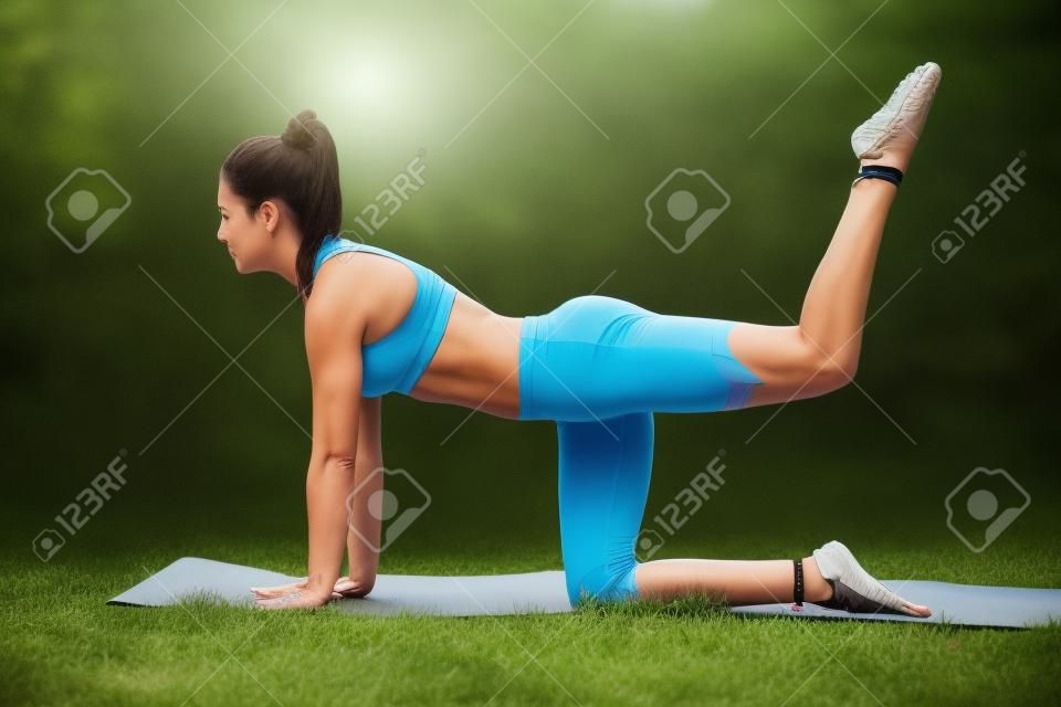 Bella donna forte bruna sportiva facendo pushup esercita su una stuoia di yoga nel parco