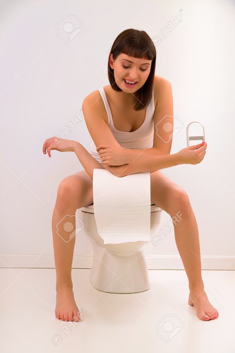 El uso del inodoro. Una joven mujer utiliza un inodoro con un rollo de papel higiénico en la mano.