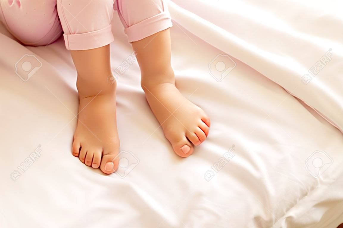 Legs of nice little girl sitting on her bed at home, close up