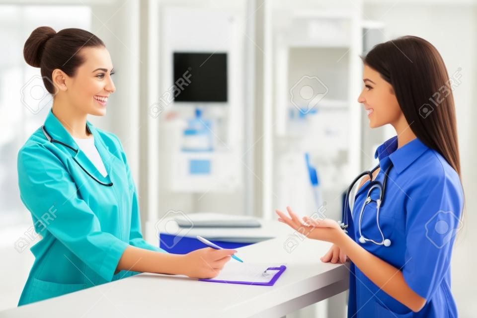 Güzel genç kadın doktor kliniğinde bekleme odasında duran, hasta ile konuşarak ve gülümseyen