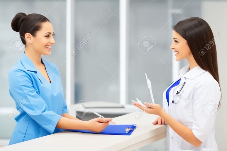 Красивая молодая женщина-врач разговаривает с пациентом и улыбается, стоя в приемной клиники
