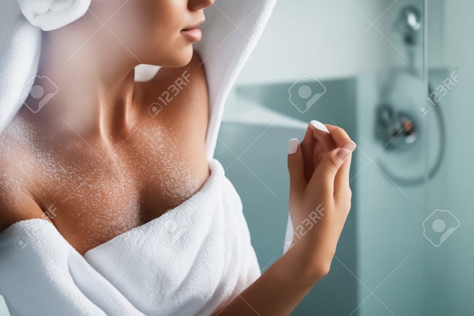 Beautiful girl in bath towel is applying deodorant while standing in bathroom after having a shower