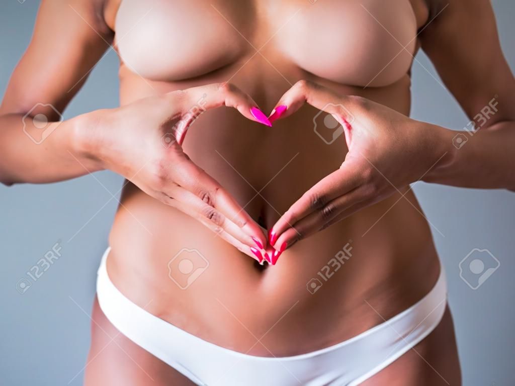 Cropped image of beautiful Afro American girl showing heart on her stomach, on gray background
